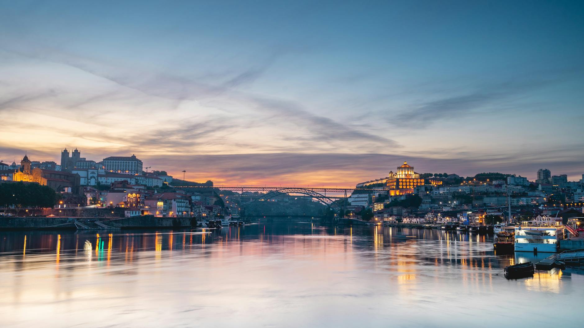 A stunning view of Porto at sunset, reflecting on the Douro River with the city skyline and iconic bridge.